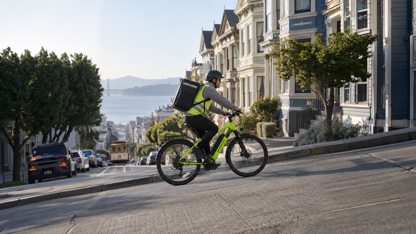 Delivery rider in a helmet and hi-vis vest riding a lime-green Whizz e-bike up a steep San Francisco street, with Victorian houses, a cable car and the bay in the background
